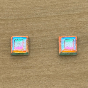 Iridescent rectangle glass earrings with green and pink top, blue and yellow center, and orange and blue bottom colors on wood background