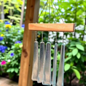 Glass wind chime with wooden top, hanging on a patio with vibrant flowers and greenery in the background.