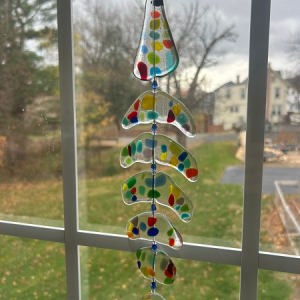 Bonefish light catcher in multicolor fused glass, hanging in window with vibrant dots and suburban backdrop